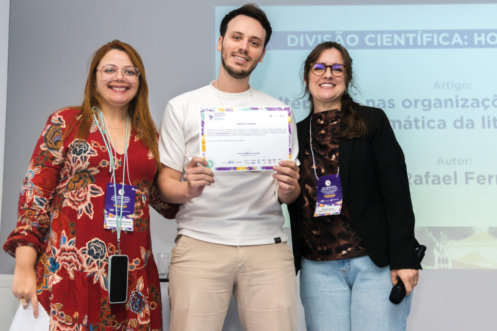 Rafael Cunha Ferro recebe a premiação de Marília, coordenadora de Comunicação da ANPTUR (à esq.) e de Mariana Bueno de Andrade-Matos, diretora científica da ANPTUR (à dir.).